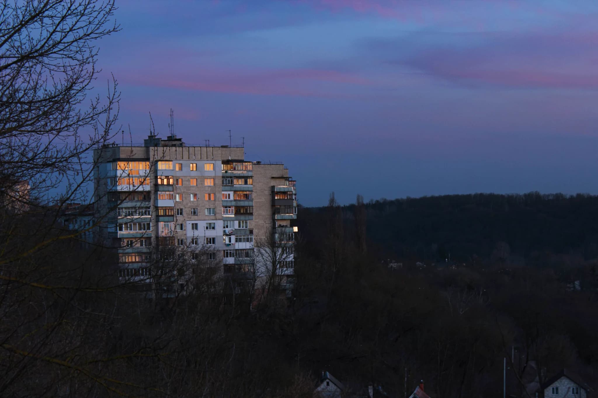 A brutalist concrete tower at dusk, haze between the floors, long lens, the last of the sun on one corner