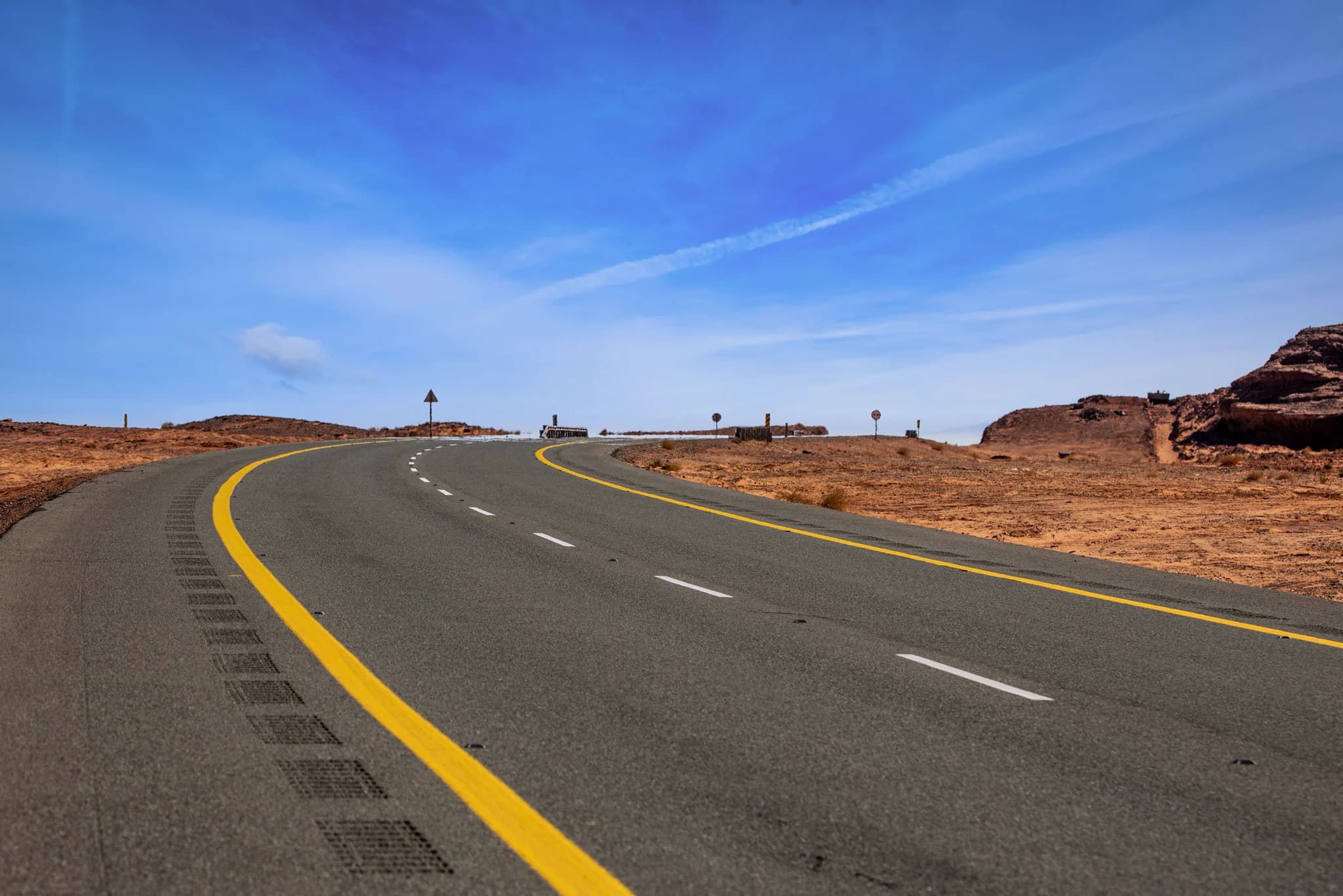 A desert highway running to a vanishing point, heat shimmer lifting off the asphalt, anamorphic flare across the frame
