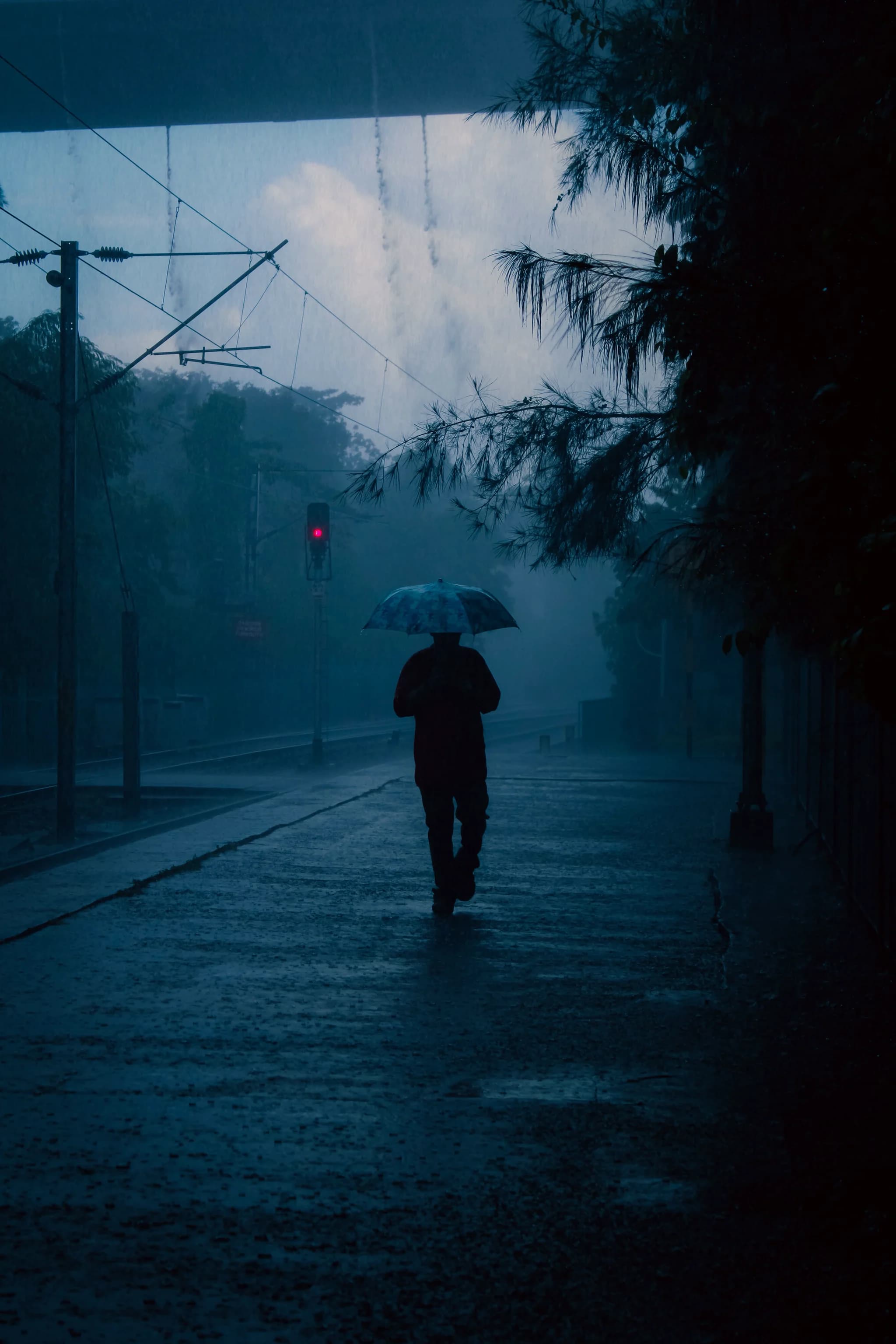 A silhouette under a sodium-vapour underpass, wet asphalt throwing the light back, deep unlit gaps